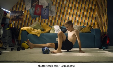 Young Athlete Boy Uses Foam Roller In His Room. Warm Up Sports Training. School Sports Team Soccer Player. Stretching Muscles. Workout At Home.