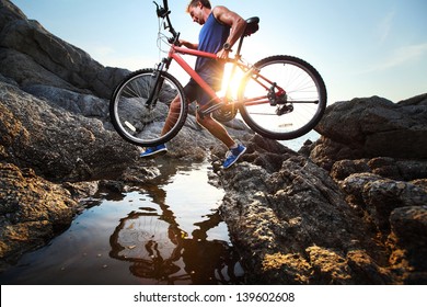 Young athlete crossing rocky terrain with bicycle in his hands - Powered by Shutterstock