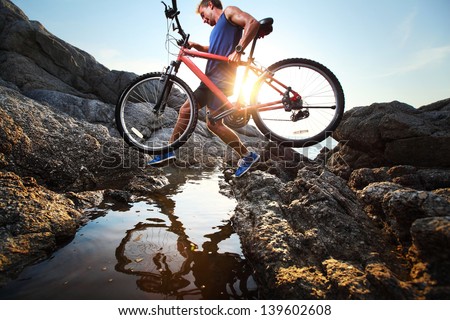 Young athlete crossing rocky terrain with bicycle in his hands
