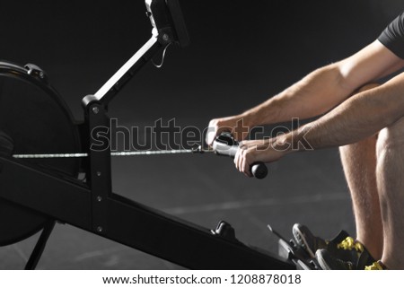 Young athlete doing rowing exercises in dark concept gym.