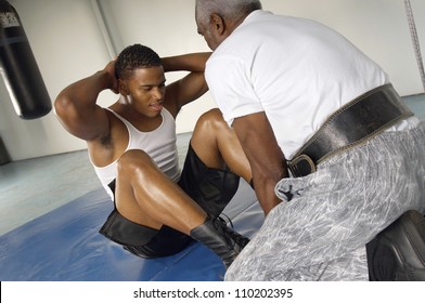 Young athlete doing sit-ups with his trainer at gym - Powered by Shutterstock