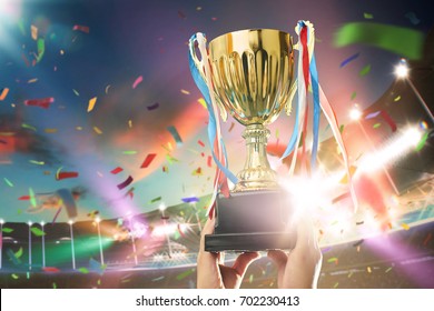 Young athlete holding up a gold trophy cup with space ready for your trophy design. Grand stadium celebration with spotlight , flare and confetti .. - Powered by Shutterstock