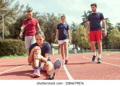 Young Athlete Injured To Knee On The Track While Being Helped By His Coach And His Teammates