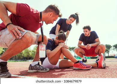 young athlete injured to knee on the track while being helped by his coach and his teammates - Powered by Shutterstock