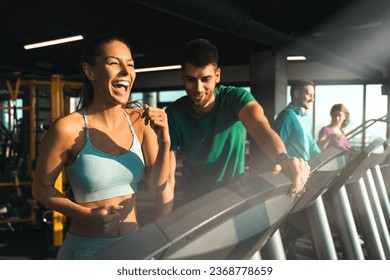 Young athlete male assisting a young woman while exercising on treadmills in a gym. Excited smiling girl running under his instructor's supervision. - Powered by Shutterstock