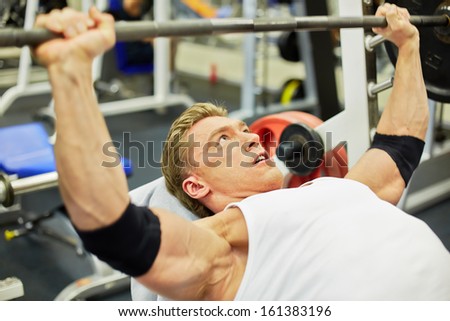 Young athlete man does bench press from chest exercise in gym hall
