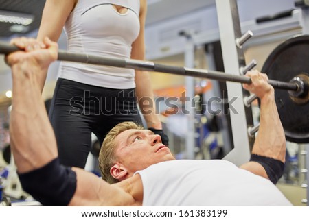 Young athlete man does bench press from chest exercise in gym hall under supervision of female coach