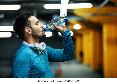 Young athlete man is drinking water after exercise in garage.