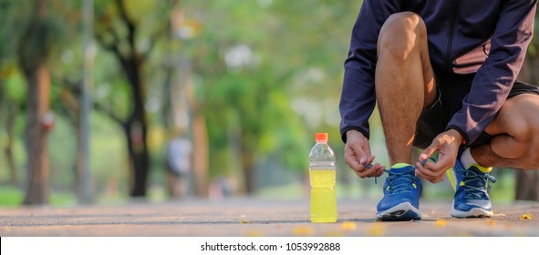 Young Athlete Man Tying Running Shoes In The Park Outdoor, Male Runner Ready For Jogging On The Road Outside, Asian Fitness Walking And Exercise On Footpath In Morning. Wellness And Sport Concepts