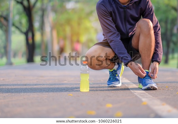 Young athlete man tying running shoes in the park outdoor, male runner ready for jogging on the road outside, olahraga dalam kegiatan rutin harian, pola hidup sehat pekerja