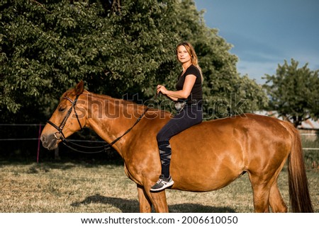 Young athlete poses on horse in the evening at ranch. Beauty and health. Life in nature. Sports and recreation.