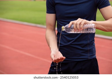 young athlete pours water on his hands from a bottle while cooling down on a running track after an intense workout session - Powered by Shutterstock