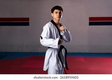 Юный спортсмен, практикующий тхэквондо в добоке и черном поясе, выполняет движение по боевым искусствам в спортзале