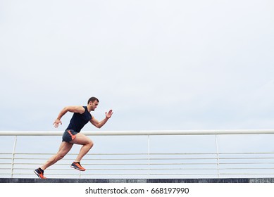 Young Athlete Running Fast Outdoors. Wearing Sport Cloth, Doing Wide Step, Demonstrating Healthy Way Of Life, Wide Shot