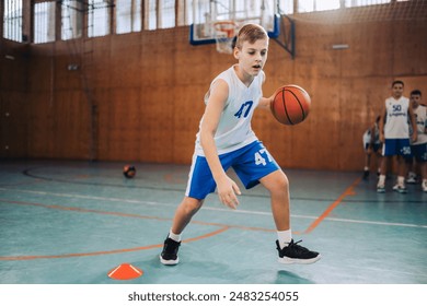 A young athlete in sportswear dribbles a basketball in a team sport practice held in an indoor gym - Powered by Shutterstock