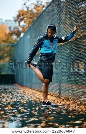 Young athlete warming up while exercising in the park during rainy day. Copy space.