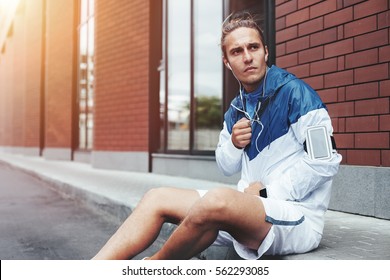 Young athlete in windrunner sitting on the street after good jogging session at sunset - Powered by Shutterstock