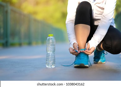 Young Athlete Woman Tying Running Shoes In The Park Outdoor, Female Runner Ready For Jogging On The Road Outside, Asian Fitness Walking And Exercise On Footpath In Morning. Wellness And Sport Concepts