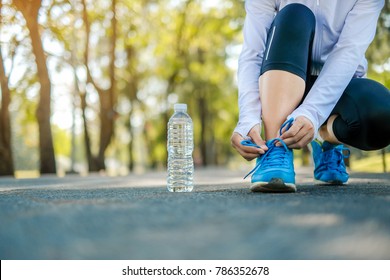 Young Athlete Woman Tying Running Shoes In The Park Outdoor, Female Runner Ready For Jogging On The Road Outside, Asian Fitness Walking And Exercise On Footpath In Morning. Wellness And Sport Concepts