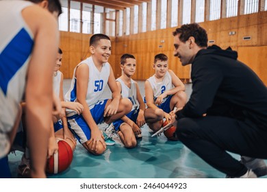 A young athletes are kneeling at indoor court with their basketball trainer and working on game strategy. Junior basketball team at indoor court having consultations with coach on their training. - Powered by Shutterstock