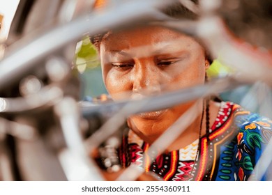 Young athletic african american female carefully looking through bike wheel for damages to repair and maintain. Detailed image of sports-loving black woman intently examining modern bicycle rim for - Powered by Shutterstock