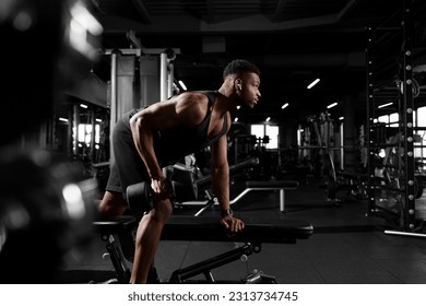 young athletic african american man trains in dark gym, athletic guy lifts heavy dumbbells in fitness club - Powered by Shutterstock