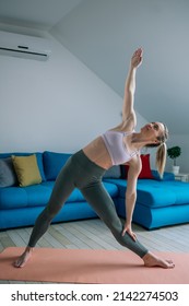 Young athletic attractive woman practicing yoga at home and doing Utthita Trikonasana exercise. Extended triangle pose. Yoga at home.