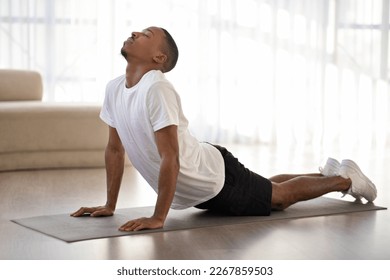 Young athletic black guy in sportswear doing morning yoga practice on fitness mat at home, stretching body, side view, copy space. Healthy lifestyle, sport, yoga concept - Powered by Shutterstock