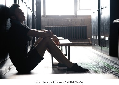 Young athletic Caucasian man sitting alone in dark gym locker room resting after workout. - Powered by Shutterstock