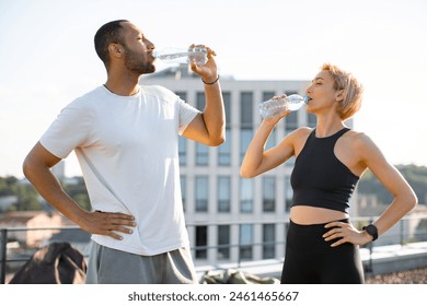 Young athletic family engaged in healthy lifestyle during morning warm-up and workout on roof of modern building. Athletic sporty man and fit woman drinking water after jogging outdoors. - Powered by Shutterstock