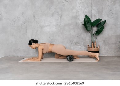 Young athletic female trainer doing fascia exercises on the floor - Caucasian woman using a foam roller - a tool to relieve back tension and relieve muscle pain.