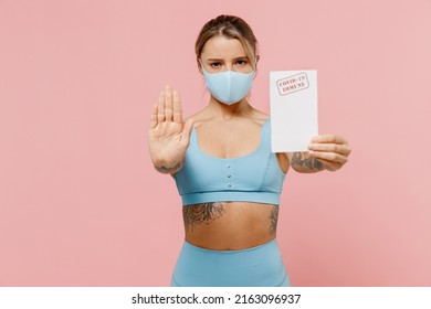 Young athletic fitness trainer instructor woman wear blue tracksuit mask spend time in home gym hold covid-19 certificate show stop gesture isolated on plain pink background. Workout sport concept.