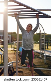 Young Athletic Fitness Woman Working Out At Outdoor Gym Doing Pull Ups At Sunrise