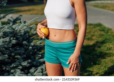 young athletic girl does massage with spiky rubber ball stomach to tighten skin and beautiful abs muscles on sunny day in park.
