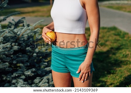 young athletic girl does massage with spiky rubber ball stomach to tighten skin and beautiful abs muscles on sunny day in park.
