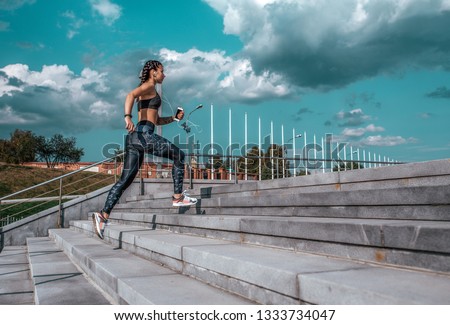 Young athletic girl running morning for jog fitness training, sportswear, leggings and top. Phone listens music headphones. Summer city workout, online playlist application to Internet. Free space.