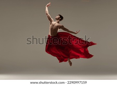 Young, athletic, handsome man, ballet dancer making performance with red silk fabric against grey studio background. Concept of art, classical dance, inspiration, creativity, beauty, choreography