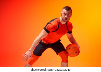 Young Athletic Man, Basketball Player Standing With Ball In Defence Position On Orange And Red Background