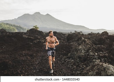 Young Athletic Man With Beard Trail Running Fast Outdoors. Topless Body And Chest Heart Rate Monitor. Mountain View On Background.