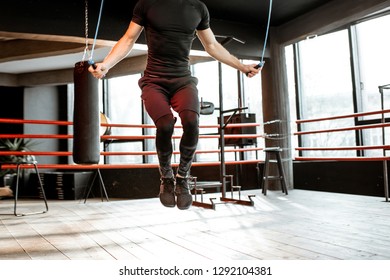 Young Athletic Man In Black Uniform Training With A Jumping Rope, Warming Up On The Boxing Ring In The Gym. Croppped Image With No Face