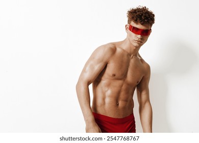 Young athletic man with curly hair wearing red sunglasses and red shorts, showing confidence and style against a plain white background. Fashion and fitness concept. - Powered by Shutterstock