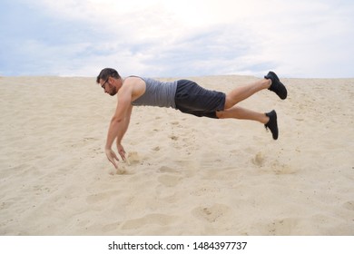 Young athletic man doing push-UPS in a jump on the sand