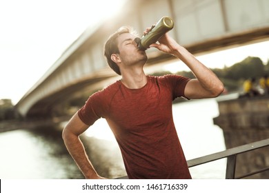 Young Athletic Man Drinking Water Or Protein Shake After Training. Recovery After Workout. Urban Outdoors Summer Scene.