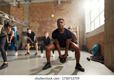 Young athletic man lifting weight while having workout at industrial gym. Group training, teamwork concept. Selective focus - Powered by Shutterstock