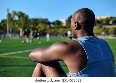 Young athletic man soccer player wear blue athletic tank top sitting on grassy sports football field, resting after game or workout. Take break, sports, lifestyle - Powered by Shutterstock