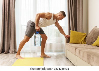 Young athletic man using big bottle of water like an alternative of dumbbell for home workout