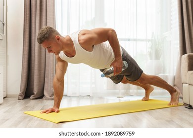 Young athletic man using bottle of water like an alternative of dumbbell for home workout