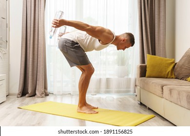 Young athletic man using bottles of water like an alternative of dumbbells for home workout