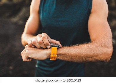 Young athletic man using fitness tracker or smart watch before run training outdoors. Close-up photo with dark background. - Powered by Shutterstock