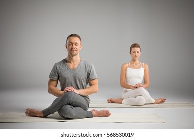 Young Athletic Man And Woman Sitting In Gomukhasana, Cow Face Pose On Yoga Mats Isolated On Grey